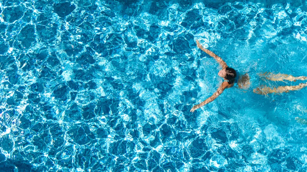 Aerial view photo of a woman with long brown hair in a blue bikini swimming in a pool. New pet-friendly apartment homes for rent with private fenced backyards in Arizona, Texas, Florida, and North Carolina with pool, pickleball, dog park, gym, clubhouse and gated community. *No breed or weight restrictions. Yardly